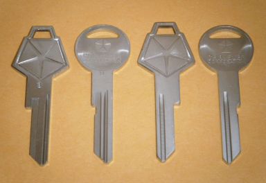 Four silver car keys with similar designs are displayed in a row on an orange surface. The keys have different shaped heads, including round and hexagonal forms, with engraved logos.